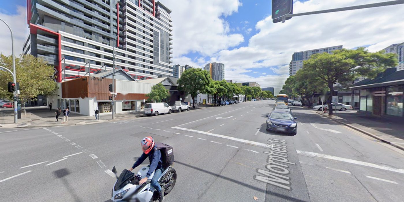 Morphett Street at Grote Street today, looking north: five lanes of traffic and turning lanes, traffic lights, an apartment tower and a row of low shops.